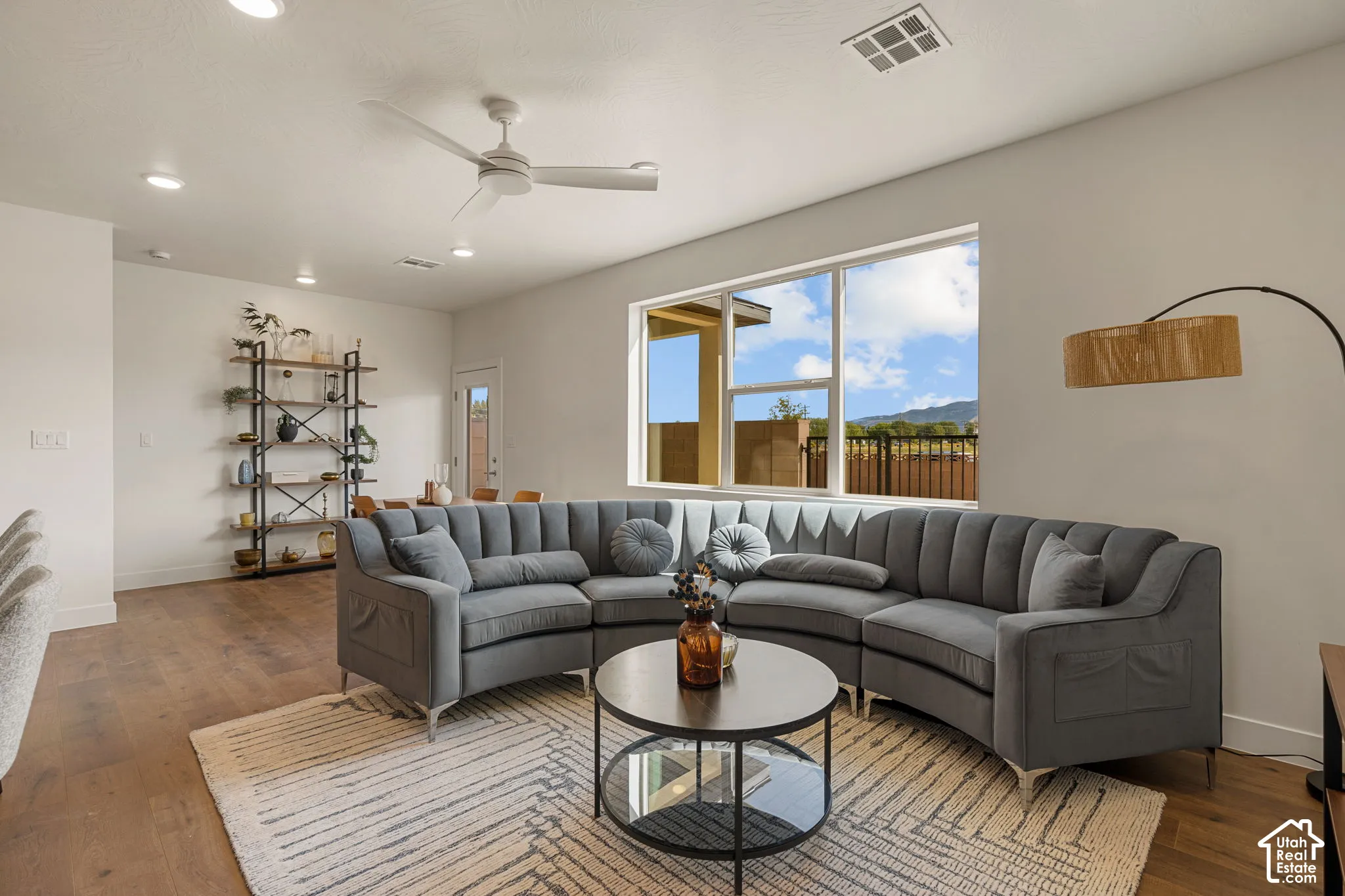Spacious living area featuring wood-finish flooring, recessed lighting, a modern ceiling fan, and large windows