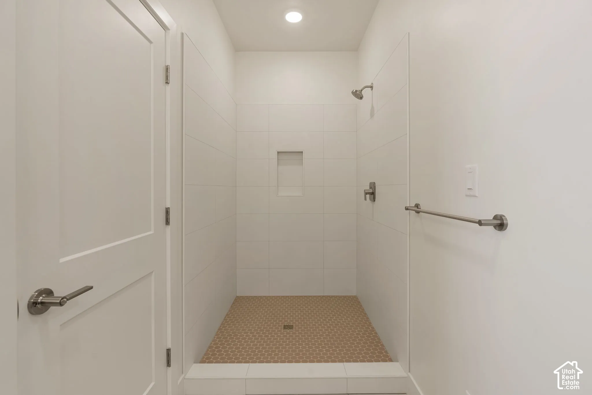 Spa-inspired walk-in shower featuring frameless glass enclosure, dual showerheads with brushed nickel fixtures, built-in niche storage, and textured tile flooring with integrated drainage