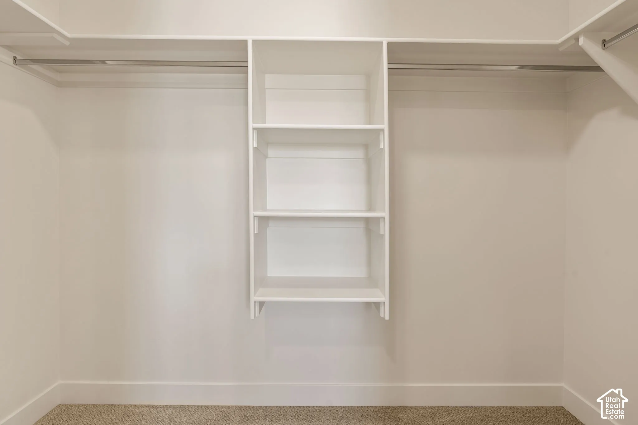 Integrated white shelving unit with three shelves, two metal hanging rods, light-toned carpeting, and crisp white walls