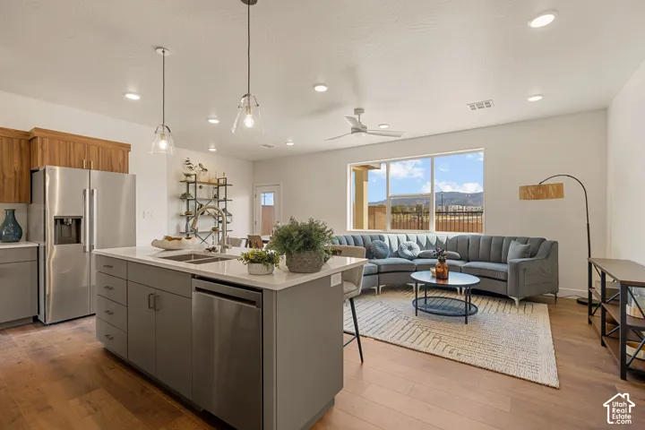 Open-concept kitchen and living area showcasing stainless steel appliances, a large island with prep space, wood-finish flooring throughout, pendant lighting, and expansive windows framing mountain scenery