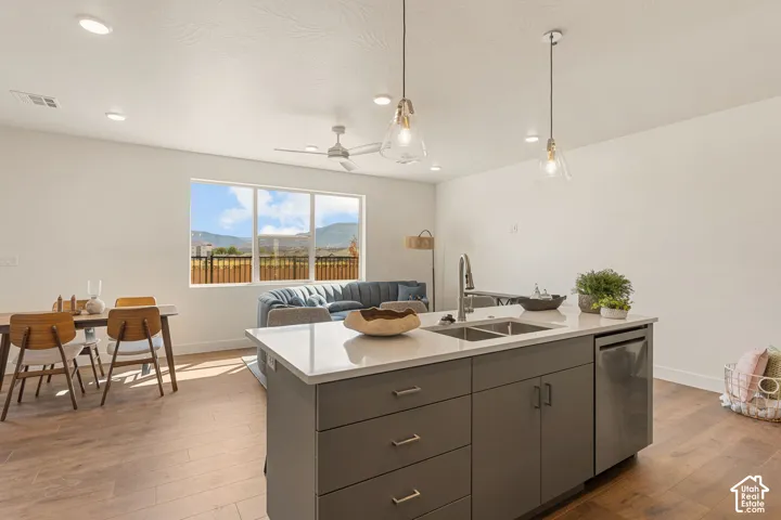 Open-concept kitchen and living area featuring a large center island with dark cabinetry and white quartz countertop, stainless steel appliances, wood-finish flooring throughout, pendant lighting, and expansive windows framing mountain scenery