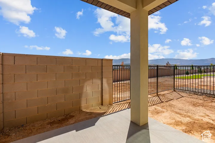 Covered patio with concrete flooring and support columns overlooking a spacious backyard featuring brick perimeter walls, metal fencing, and expansive open grounds with clear sightlines across the property