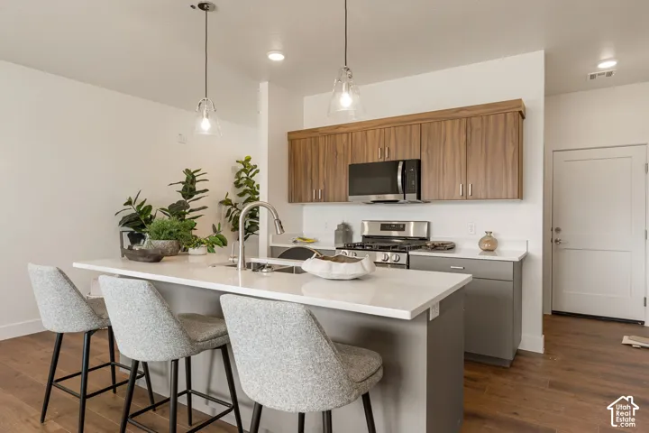 Modern kitchen and dining island featuring warm wood-finish cabinetry, stainless steel appliances, quartz countertops, pendant lighting, and upholstered seating for three