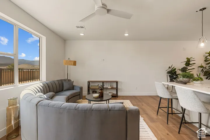 Open-concept living area showcasing hardwood flooring, a curved upholstered sofa, and abundant natural light from expansive glass doors and windows