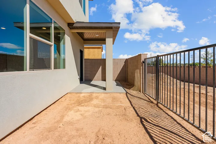 Stucco exterior with large windows, covered patio featuring a wood-finish ceiling, and a black metal fence with a gate