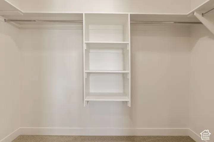 Integrated white shelving unit with three shelves, two metal hanging rods, light-toned carpeting, and crisp white walls