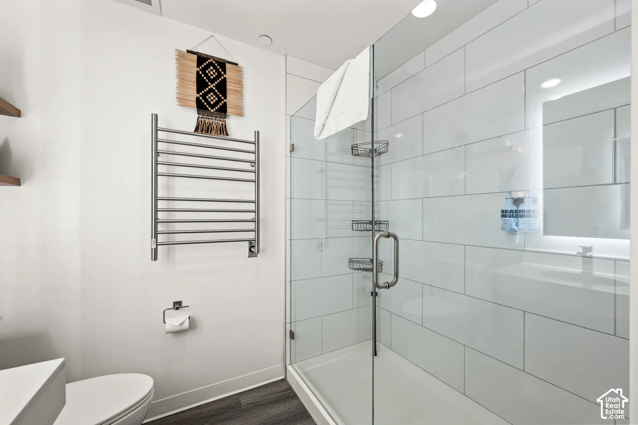 Contemporary bathroom featuring a glass-enclosed shower, white subway tile, and dark wood-finish flooring