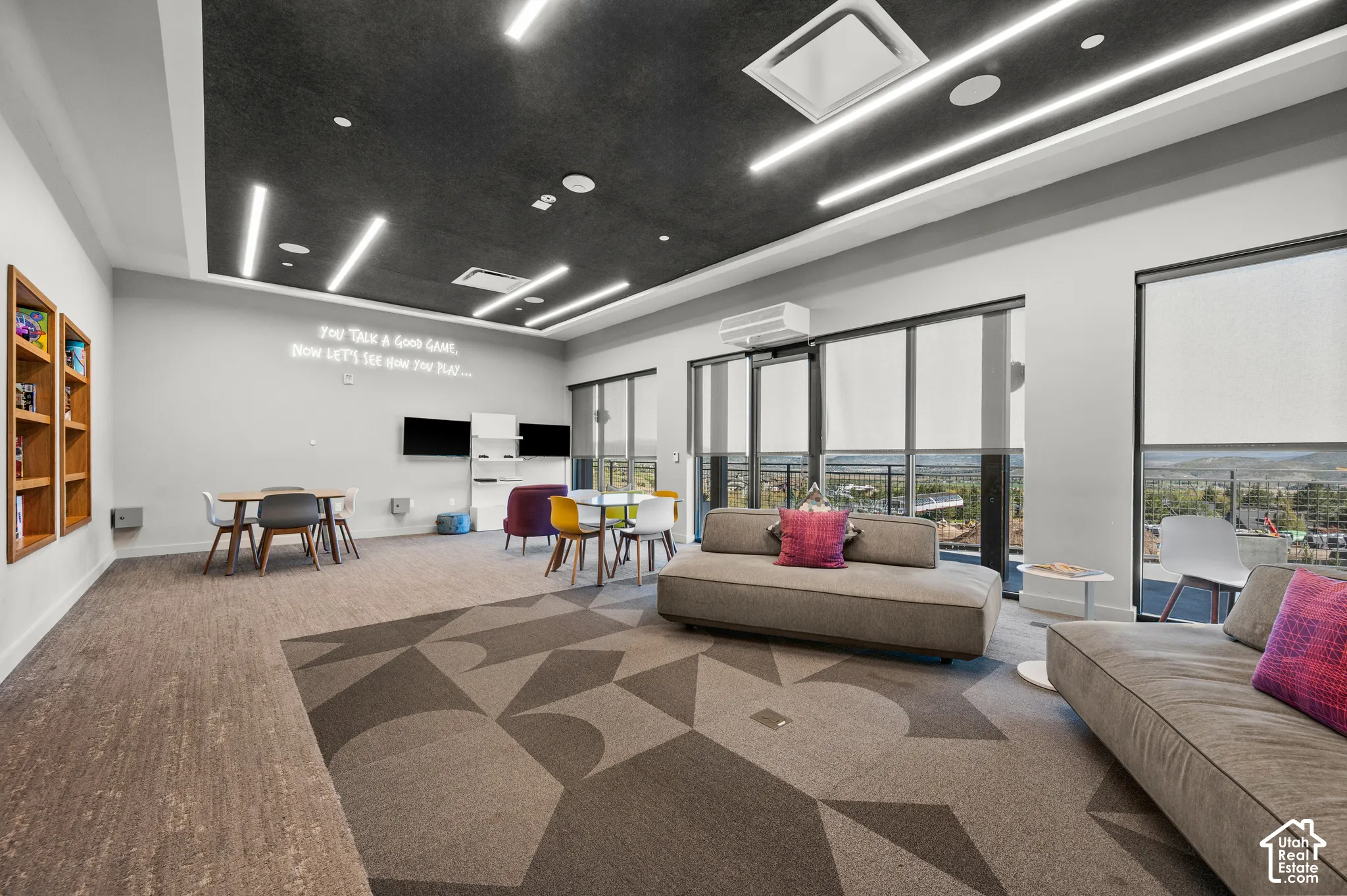 Recessed lighting and linear fixtures illuminate a carpeted common area with a geometric pattern