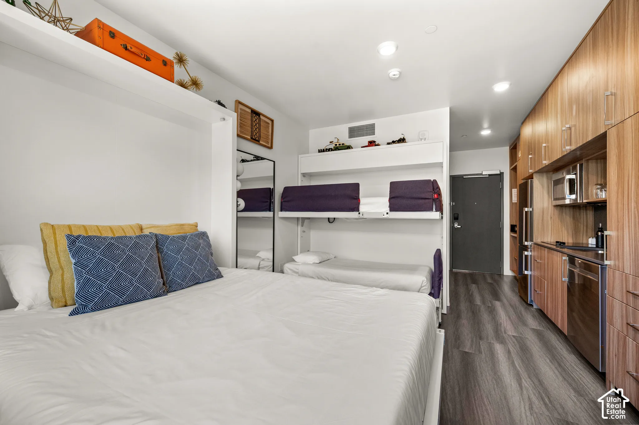 Compact living space featuring wood-finish flooring, a full kitchen with stainless steel appliances, integrated cabinetry, and built-in bunk beds