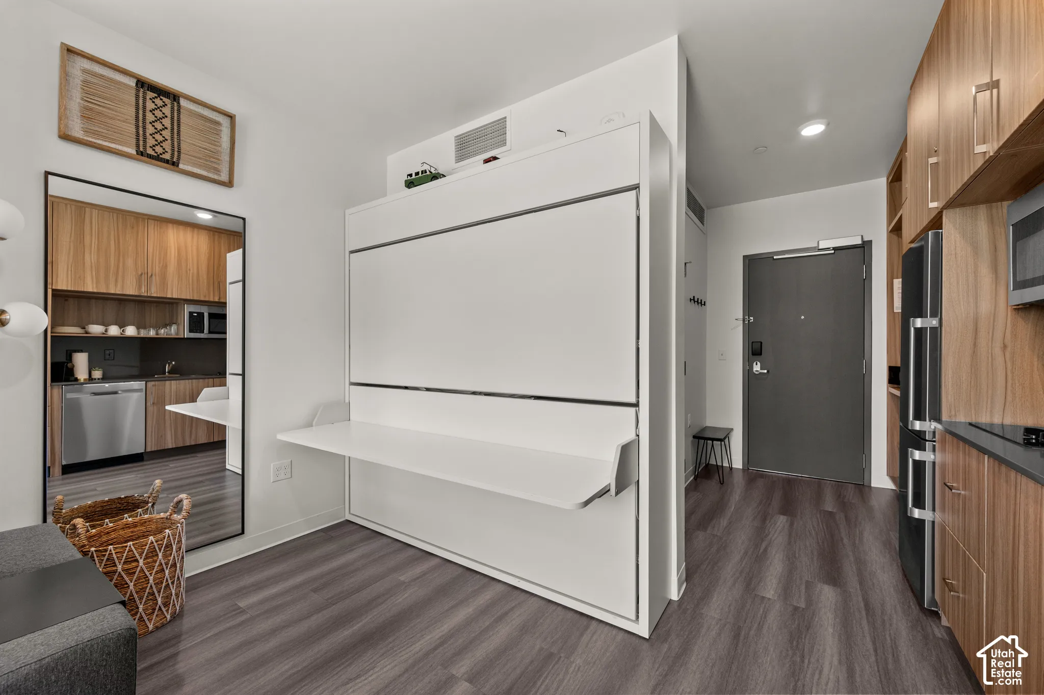 Built-in wall bed with integrated desk, wood-finish flooring, full-length mirror, wood-finish cabinetry, and stainless steel appliances