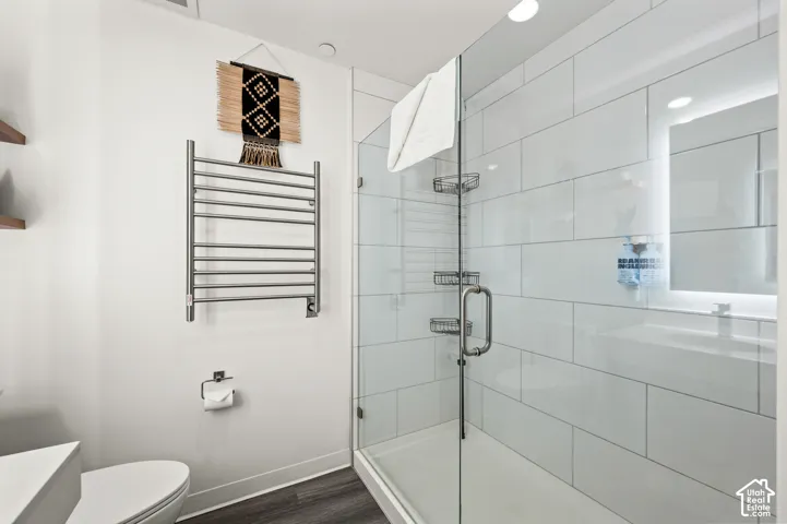 Contemporary bathroom featuring a glass-enclosed shower, white subway tile, and dark wood-finish flooring
