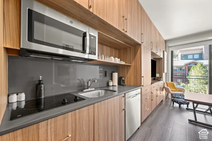Integrated kitchenette featuring wood-finish cabinetry, stainless steel appliances, and a compact dishwasher