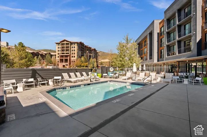 Outdoor swimming pool with integrated steps, surrounded by a concrete patio, a privacy fence, and an adjacent multi-story building