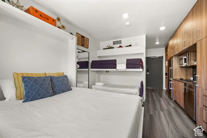 Compact living space featuring wood-finish flooring, a full kitchen with stainless steel appliances, integrated cabinetry, and built-in bunk beds