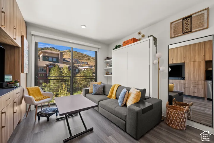 Floor-to-ceiling sliding glass doors, balcony with metal railing, built-in wall unit with wood-finish cabinetry, integrated murphy bed system, and dark wood-finish flooring