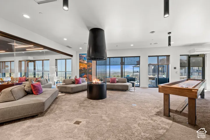 Open-concept common area featuring a suspended fireplace, expansive window walls, recessed lighting, and durable carpet flooring