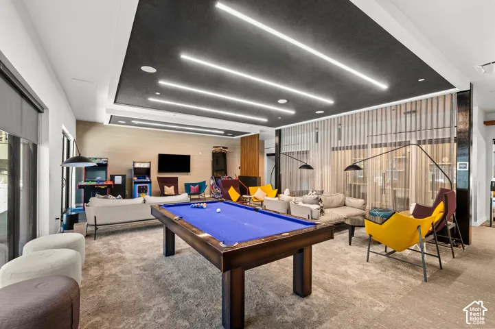 Spacious lounge area featuring a billiards table, recessed linear lighting, textured accent wall, and sheer window treatments
