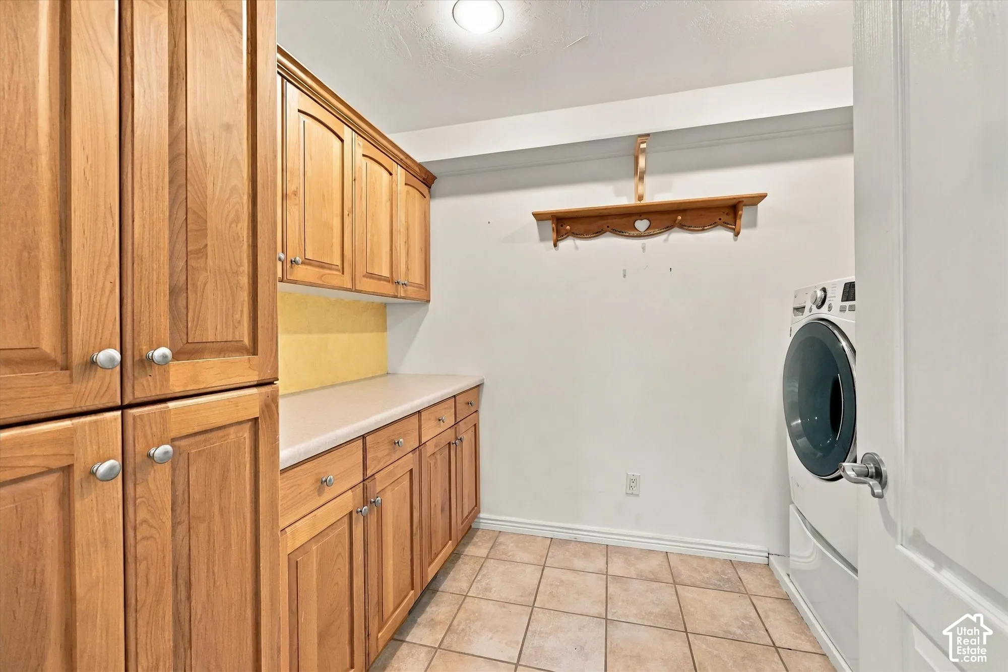 Wood-finish cabinetry with brushed nickel hardware, light-toned countertop, and tiled flooring
