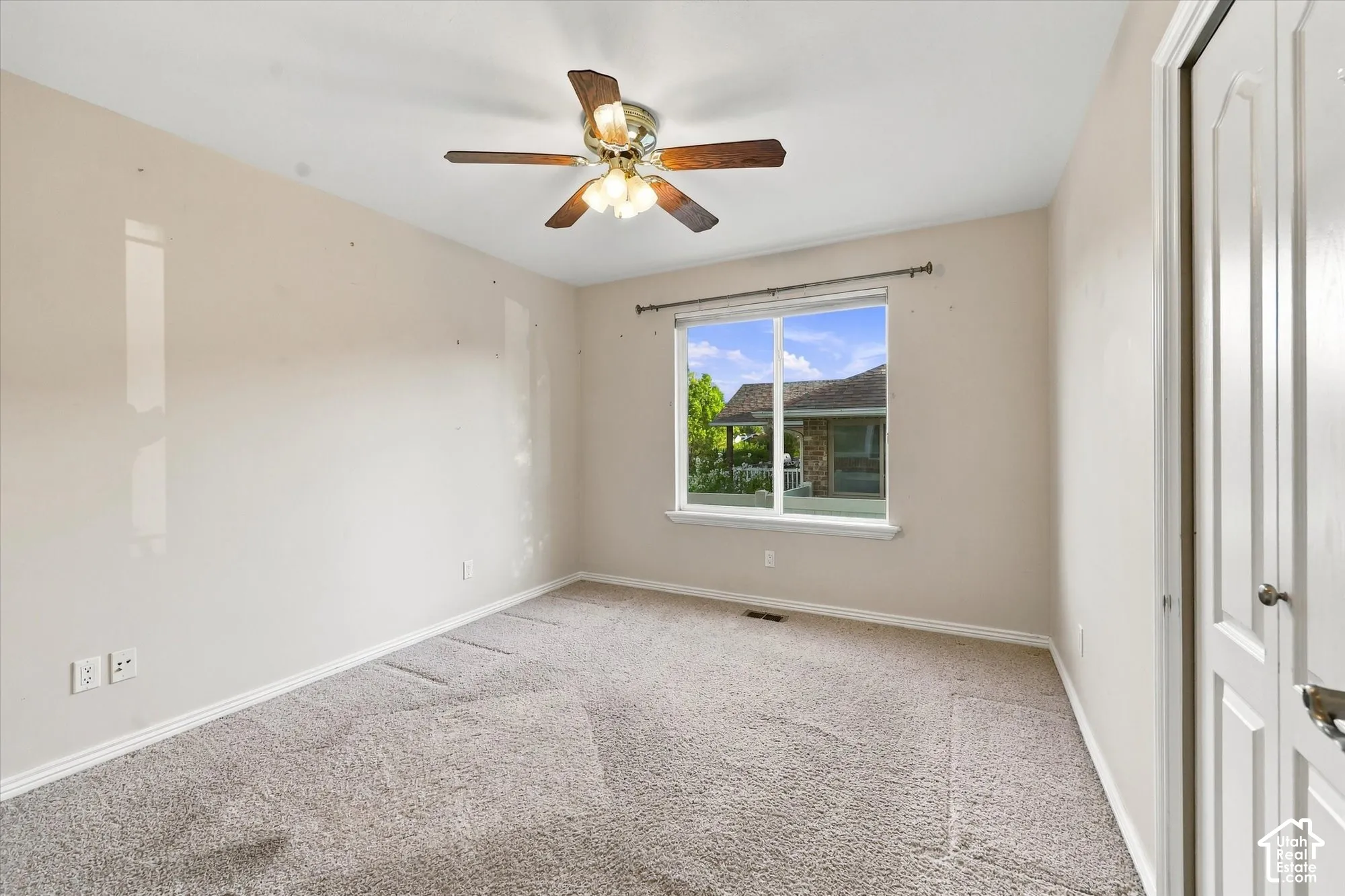 Neutral wall paint, carpet flooring, a ceiling fan with light fixture, and a window with white trim