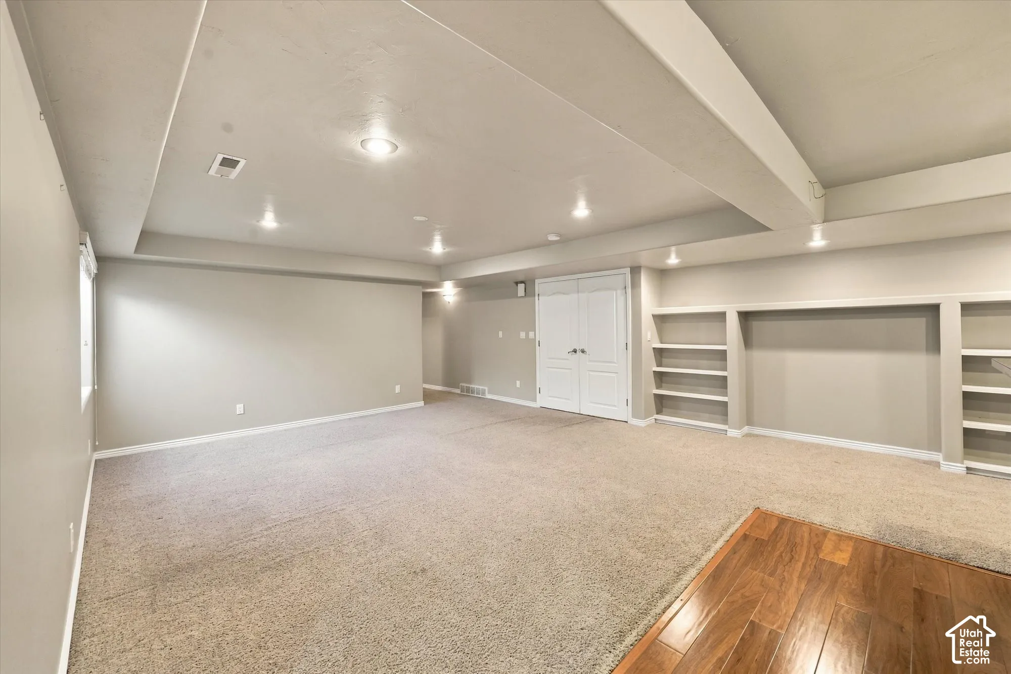 Spacious finished basement with recessed ceiling lighting, built-in shelving along perimeter walls, and mixed flooring including wood-finish hardwood and neutral carpet throughout