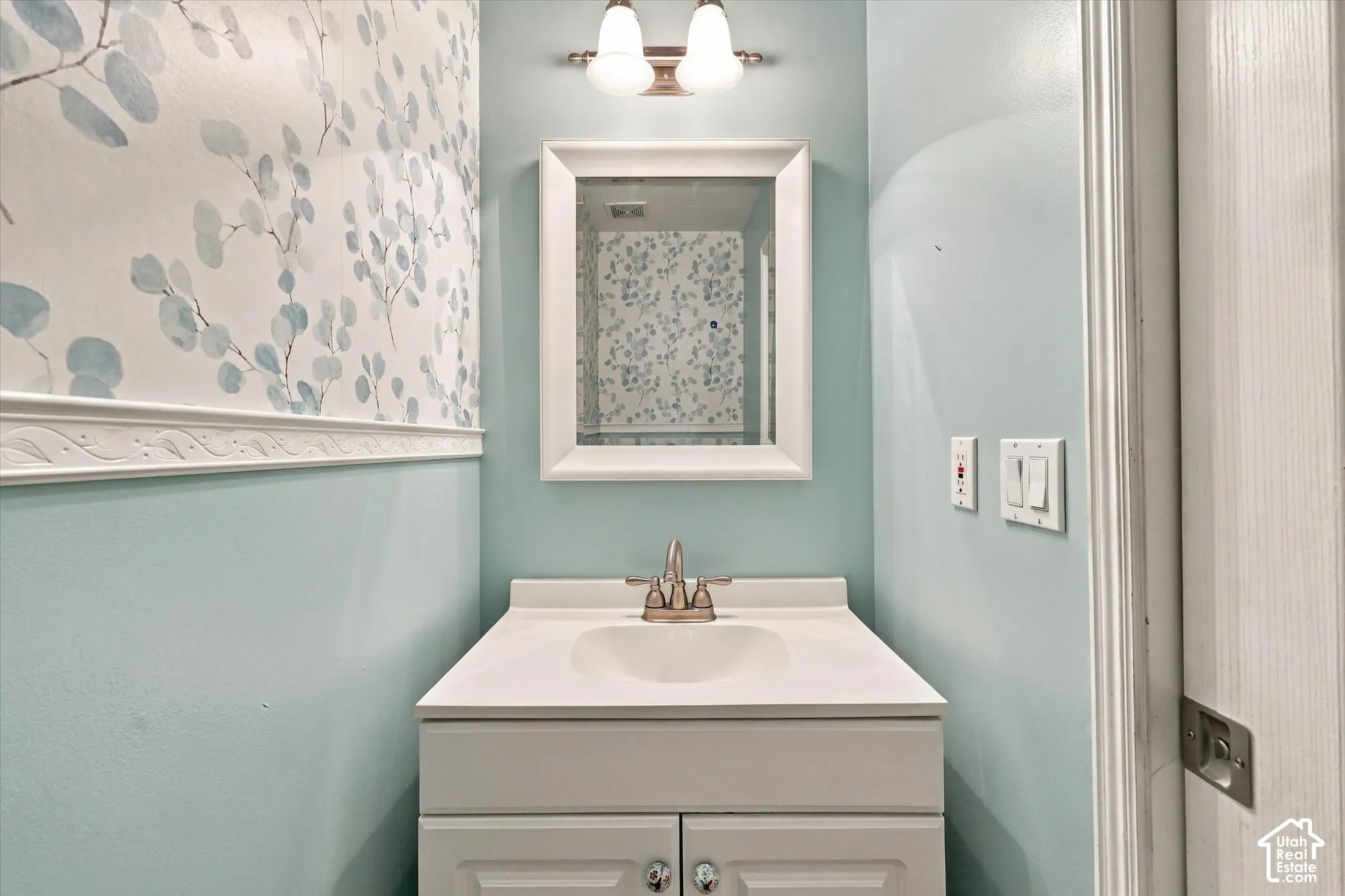 Bathroom vanity with integrated sink, brushed nickel faucet, wall-mounted mirror, and decorative wall paneling