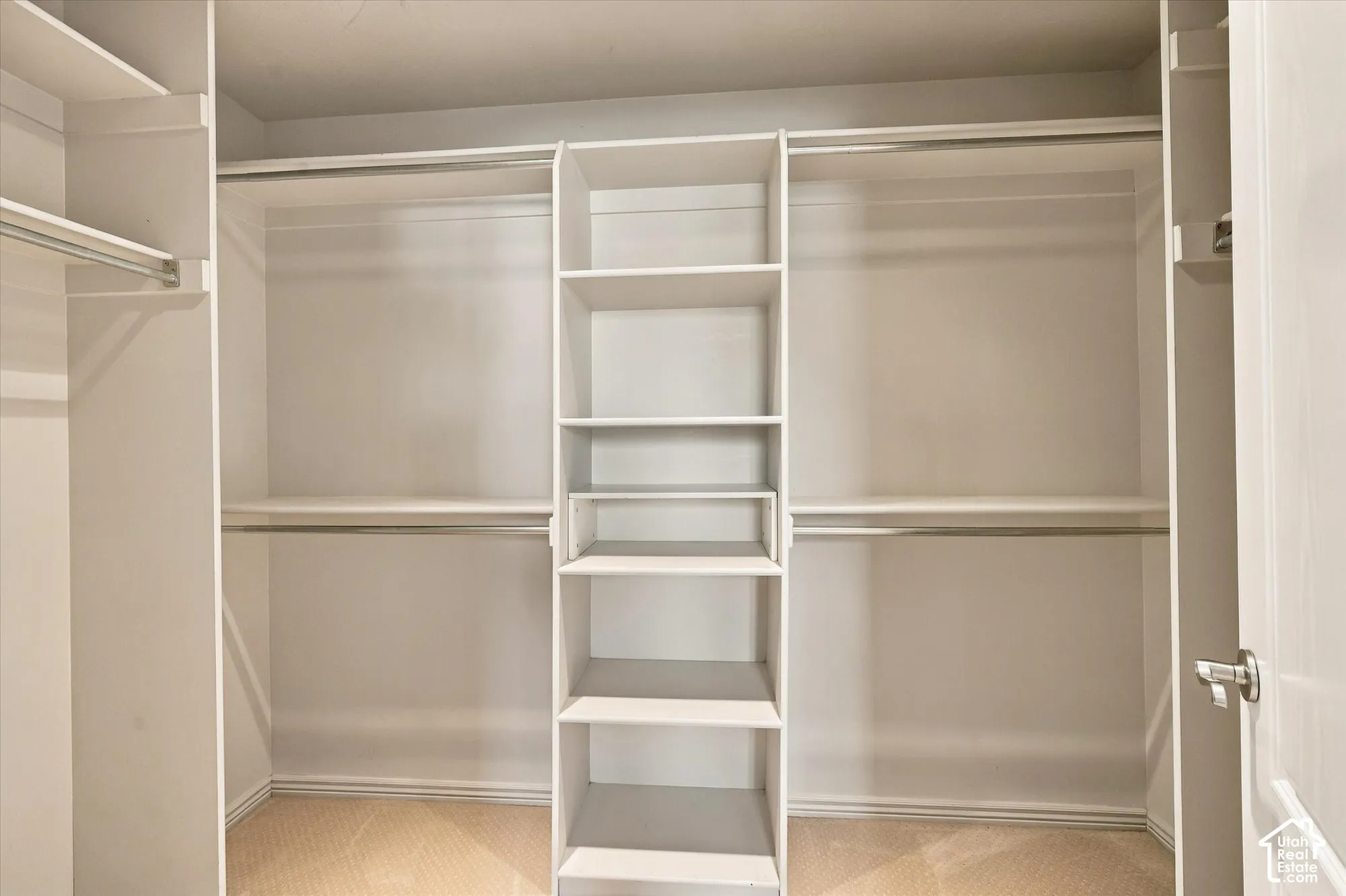 Spacious walk-in closet featuring dual hanging rods with multiple shelving sections, a center tower with built-in shelves for organized storage, and wood-finish flooring throughout