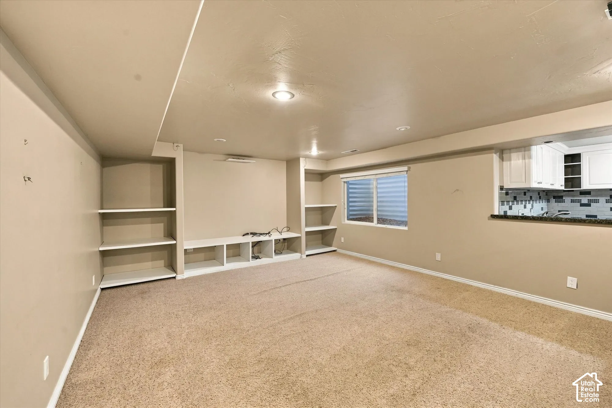 Recessed lighting, built-in shelving, built-in media console, full-size window, and a kitchen pass-through with white cabinetry and a tiled backsplash