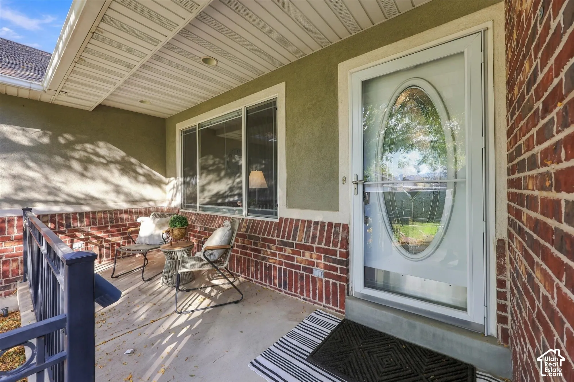 Covered porch featuring a brick facade, stucco siding, and a white storm door with an oval glass insert