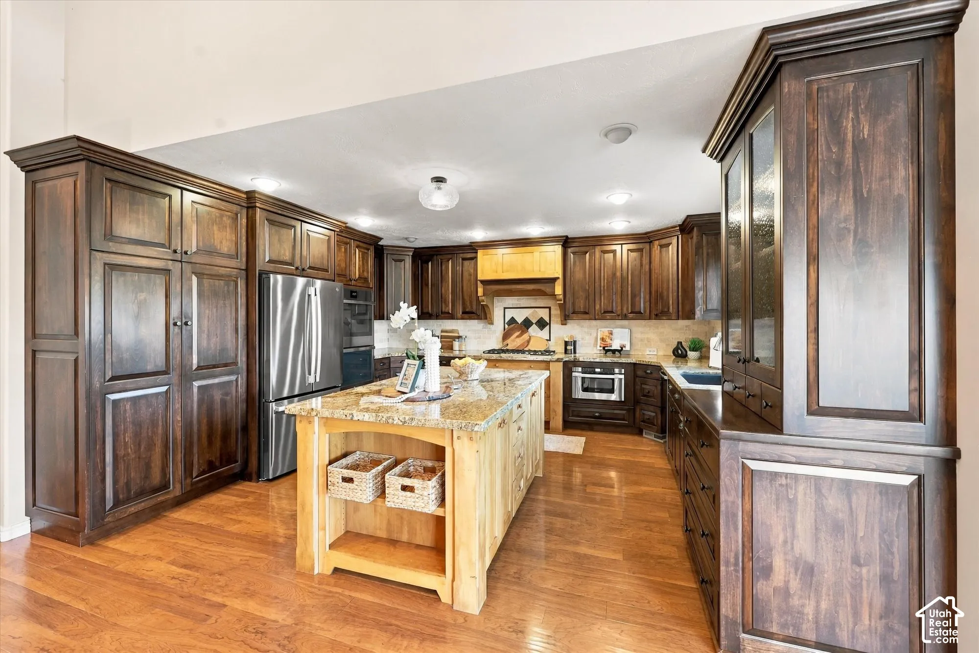 Hardwood flooring, wood cabinetry with crown molding, stainless steel appliances, granite countertops, and a wood kitchen island with shelving