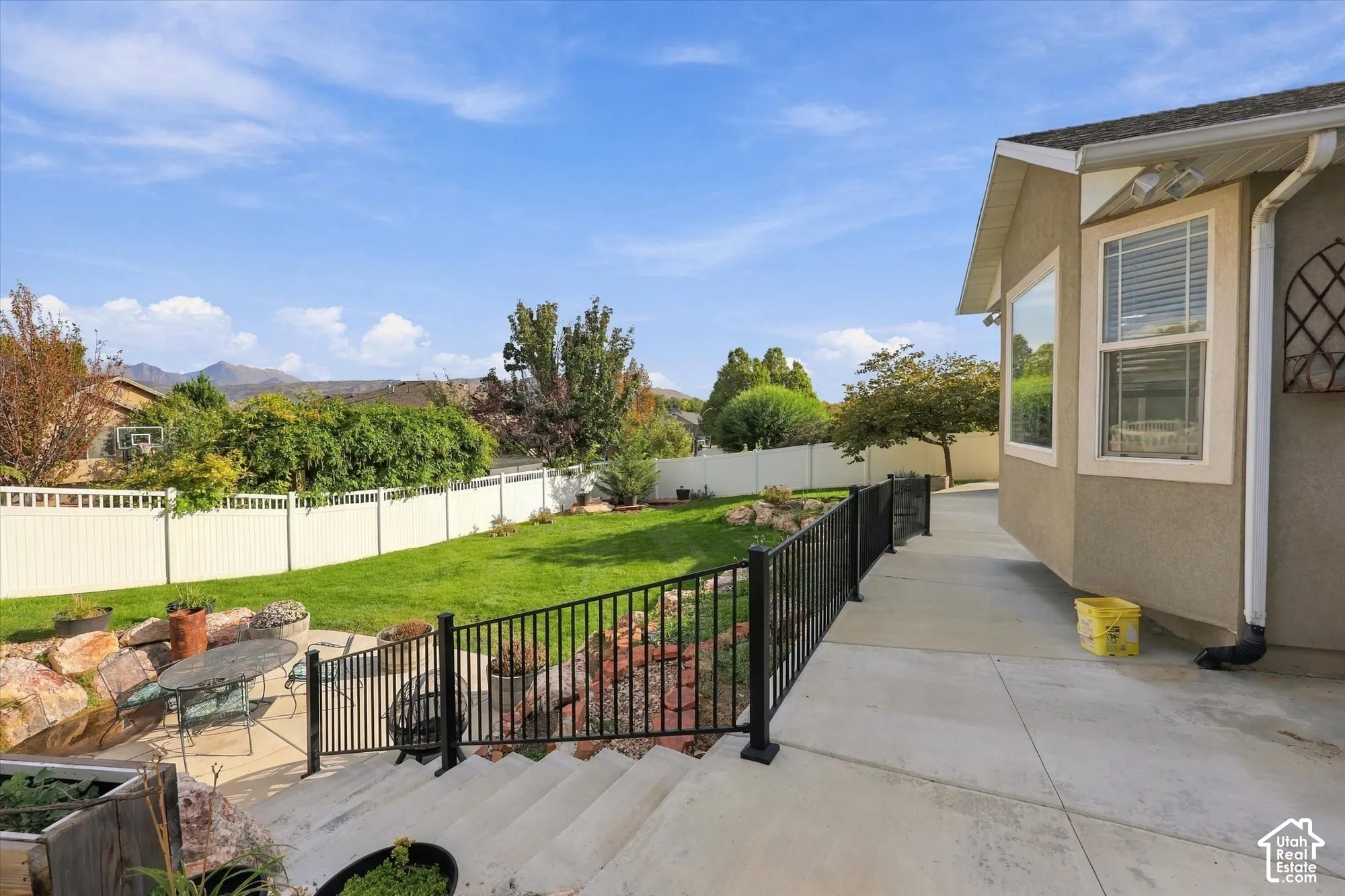 Expansive backyard featuring a manicured lawn, mature landscaping, and black metal railing along the patio