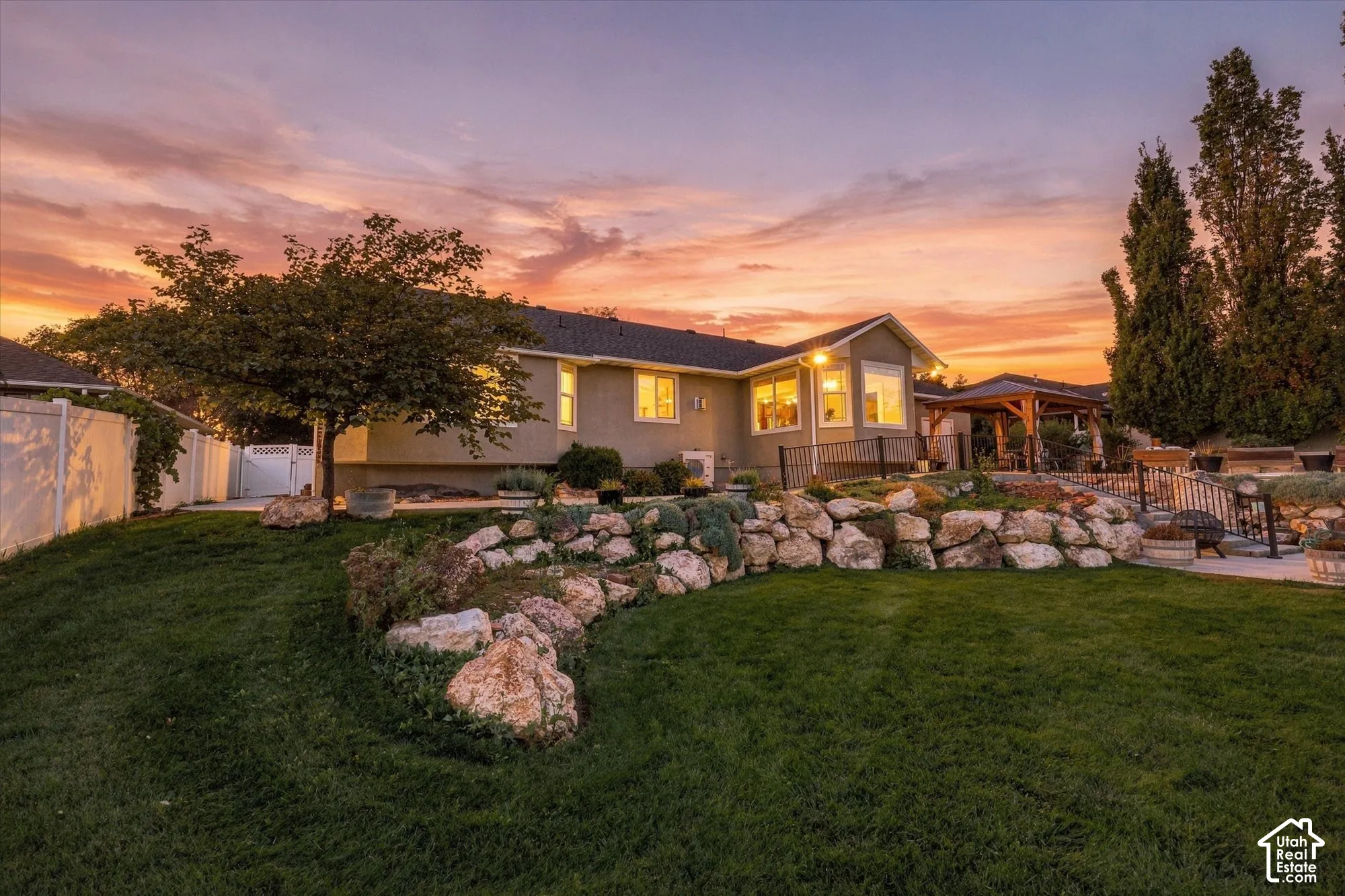 Expansive lawn with a tiered rock retaining wall, featuring a covered pergola and a fenced perimeter