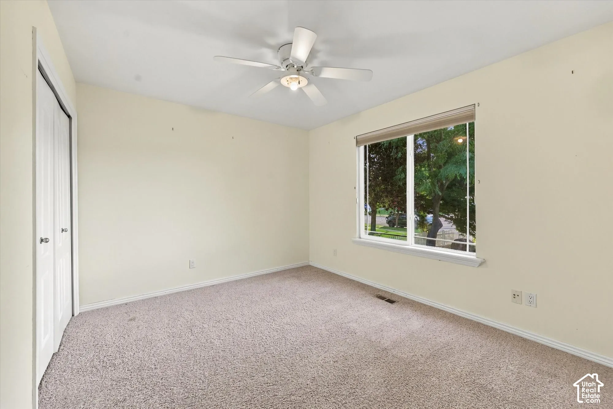 Neutral-toned wall paint, carpet flooring, a ceiling fan with integrated lighting, and a window with roller shades
