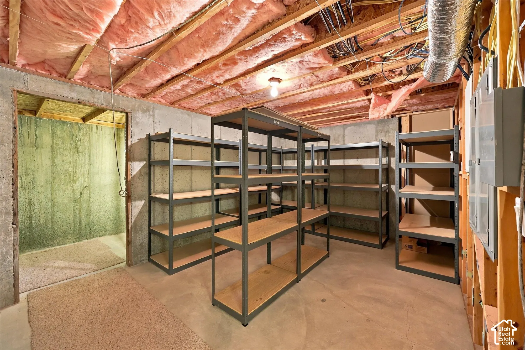 Unfinished basement featuring exposed ceiling infrastructure with copper piping, concrete flooring, and multiple industrial-style metal shelving units with wood-finish shelves