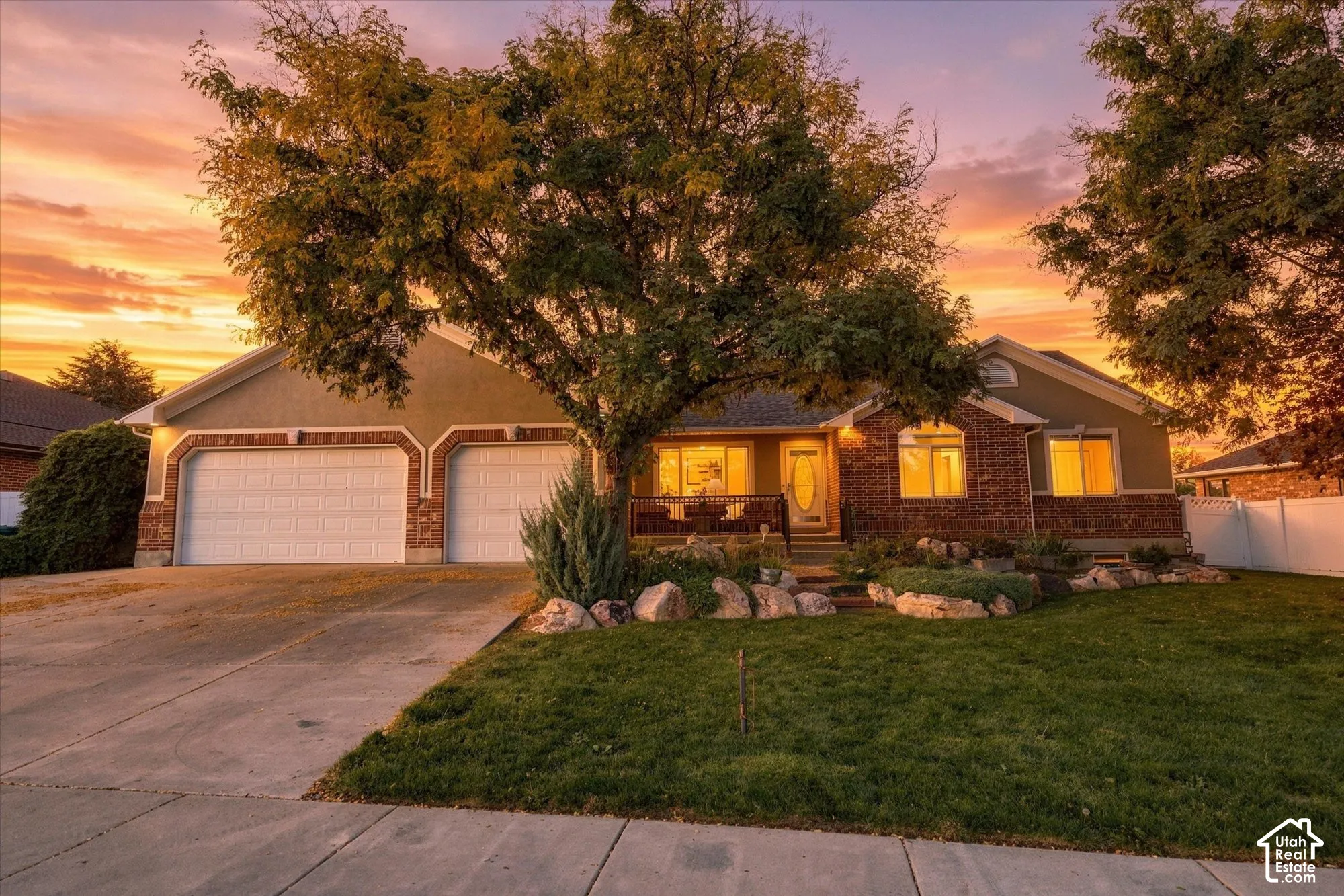 Brick single-story residence with dual-car garage, illuminated by warm interior lighting at dusk