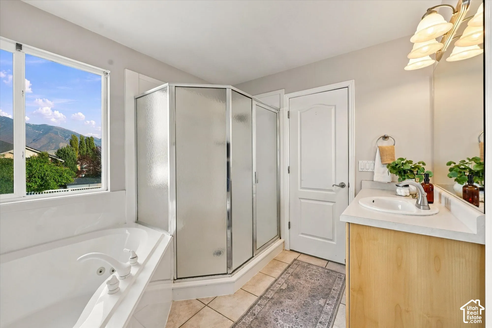 Soaking tub, walk-in shower with frosted glass, single vanity with wood-finish cabinetry, tile flooring, and a large window