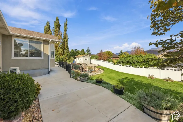 Expansive concrete patio with a black metal railing, leading to a landscaped yard with a rock feature and a white privacy fence
