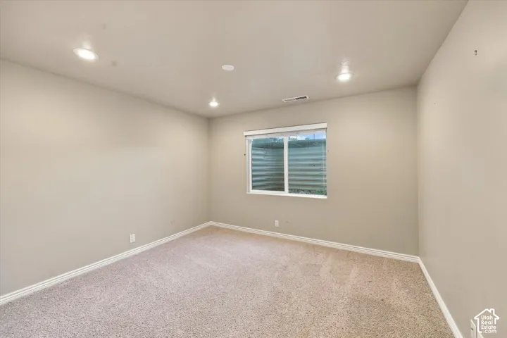 Bright, neutral bedroom showcasing recessed ceiling lighting, neutral carpet flooring, and a large window with louvered shutters providing natural light and privacy control