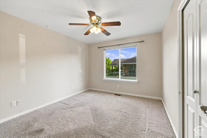 Neutral wall paint, carpet flooring, a ceiling fan with light fixture, and a window with white trim
