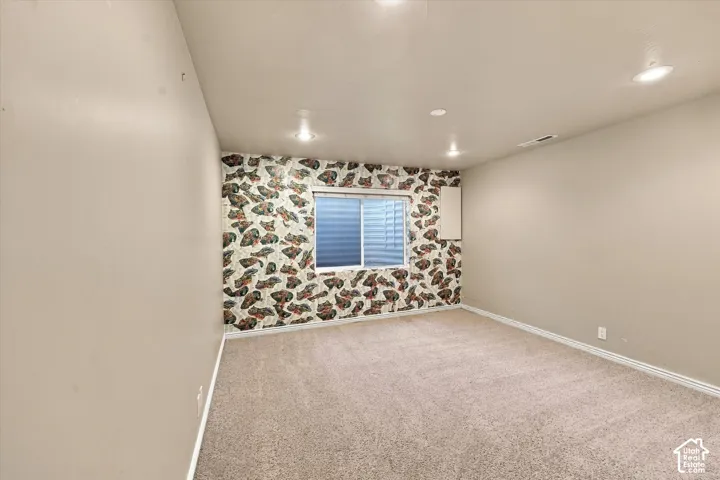 Bright bedroom showcasing neutral wall finishes, recessed ceiling lighting, carpet flooring, and a window with blue exterior shutters