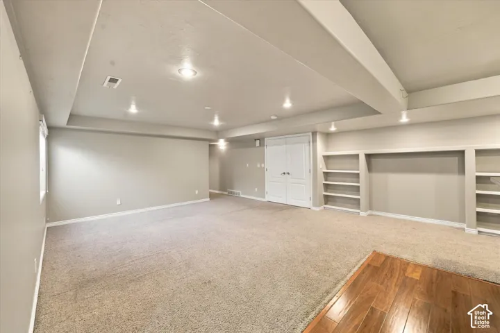 Spacious finished basement with recessed ceiling lighting, built-in shelving along perimeter walls, and mixed flooring including wood-finish hardwood and neutral carpet throughout