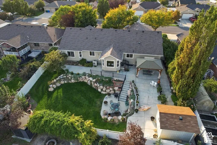 Expansive backyard featuring a manicured lawn, established landscaping, terraced hardscaping, a covered patio area, and a detached shed