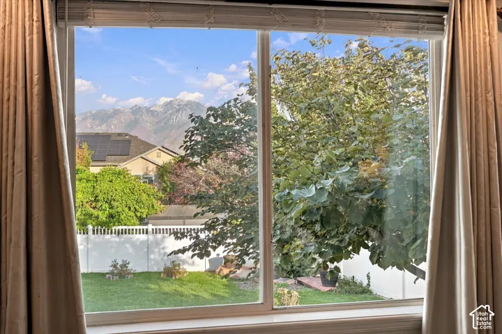 Expansive window showcasing a private backyard, mature trees, manicured lawn, and distant mountains