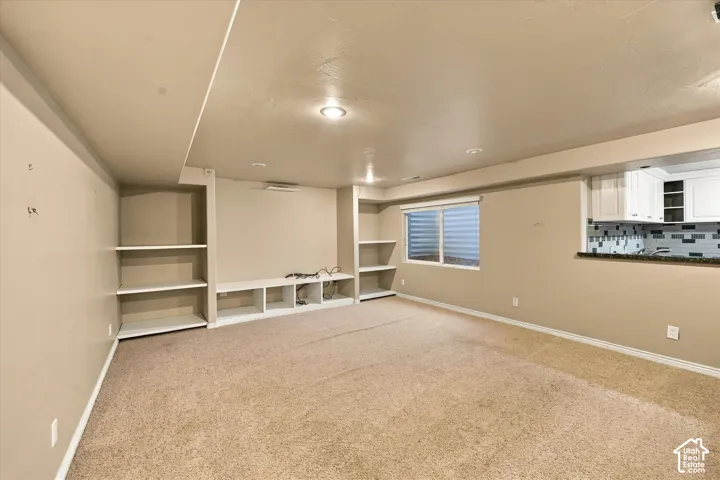 Recessed lighting, built-in shelving, built-in media console, full-size window, and a kitchen pass-through with white cabinetry and a tiled backsplash
