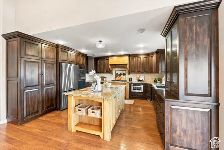 Hardwood flooring, wood cabinetry with crown molding, stainless steel appliances, granite countertops, and a wood kitchen island with shelving