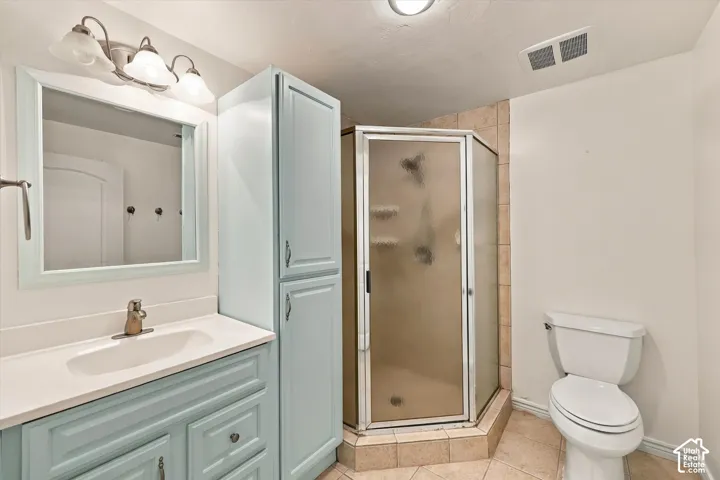 Spa-inspired bathroom featuring a light blue vanity with dual drawers, white quartz countertop, framed mirror with sconce lighting, corner shower enclosure with bronze-tone framing, and ceramic tile flooring