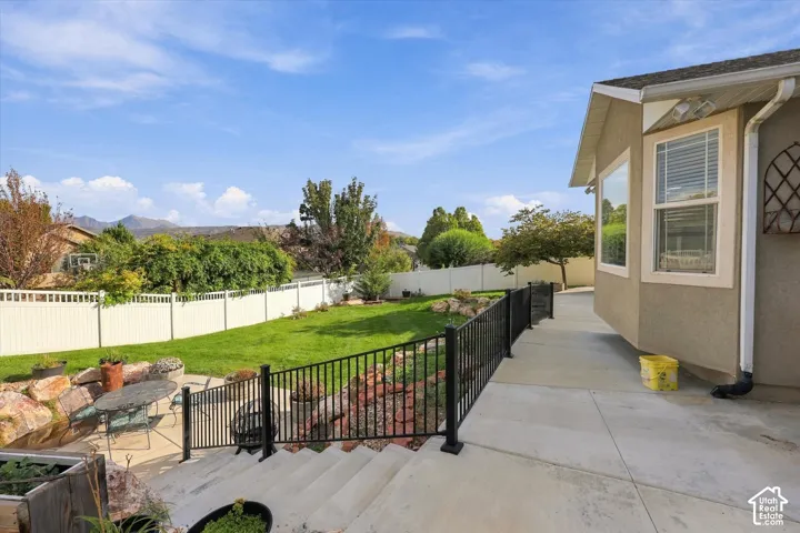 Expansive backyard featuring a manicured lawn, mature landscaping, and black metal railing along the patio