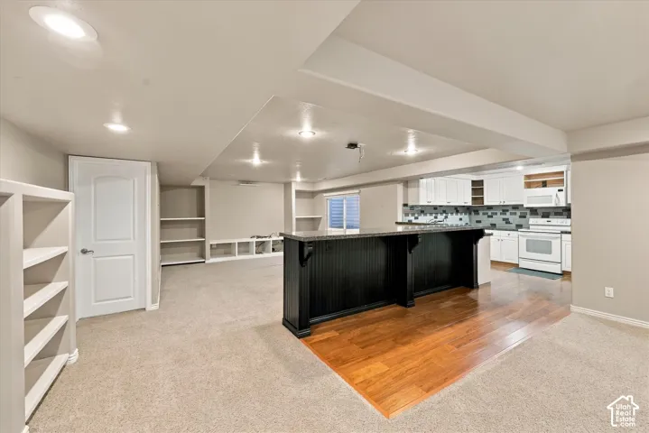 Recessed lighting, built-in shelving, a kitchen island with dark beadboard paneling, wood-finish flooring, and white cabinetry