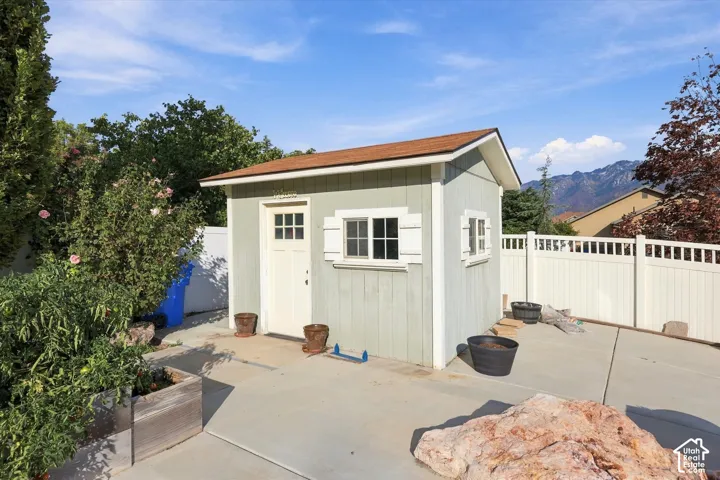 Light-colored storage shed with a brown shingle roof, white trim, and a white paneled door