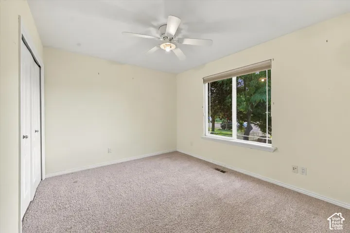 Neutral-toned wall paint, carpet flooring, a ceiling fan with integrated lighting, and a window with roller shades