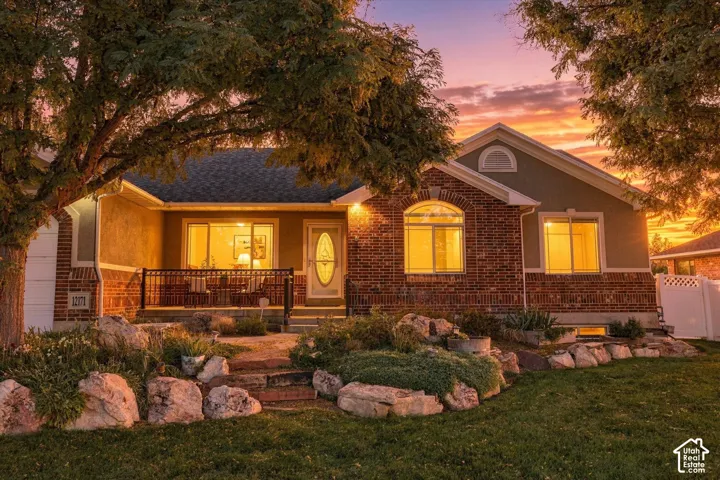 Brick and stucco exterior with multiple windows, arched window detail, covered front porch, and established landscaping